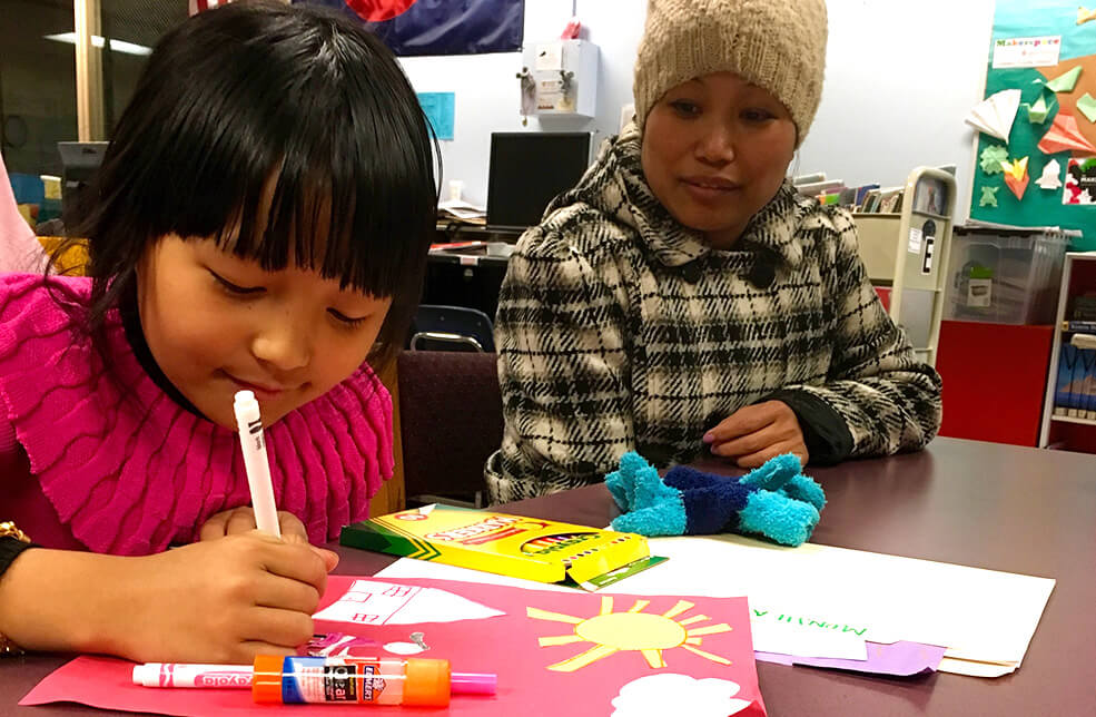 A Nepali girl holding a crayon with her mother watching her