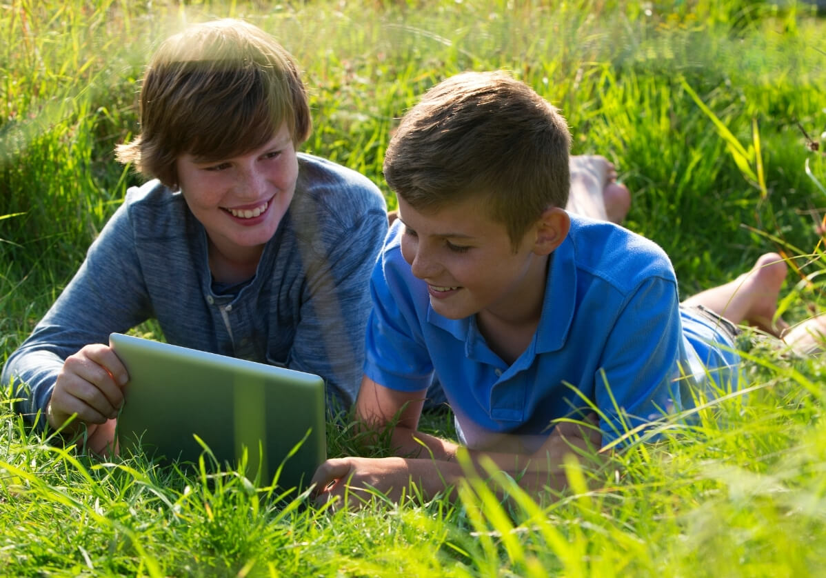 Two kids using a tablet in a field of grass