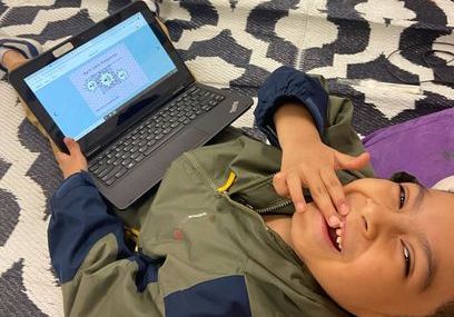 Two students smiling while using a laptop in a library